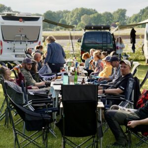 Camper sitzen an einer langen Tafel zum Abendessen beim All in Campertreffen