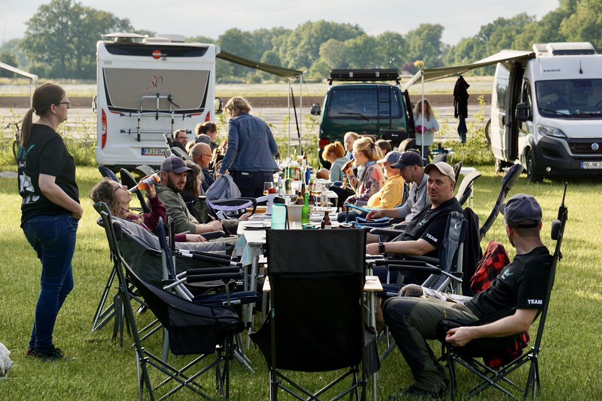 Camper sitzen an einer langen Tafel zum Abendessen beim All in Campertreffen